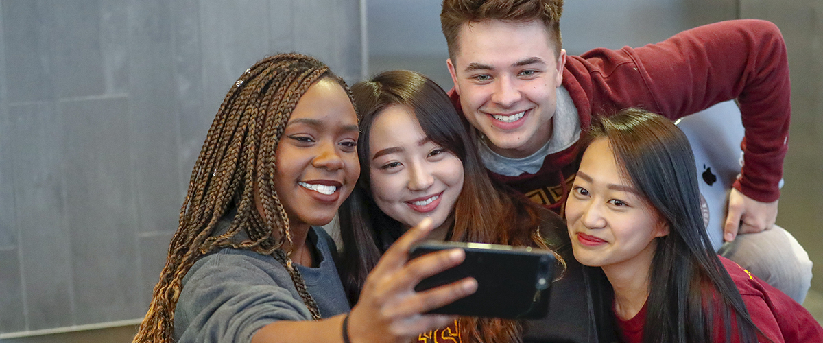 Four students gather to take a cell phone selfie