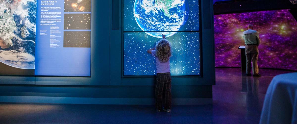 Small child engages with interactive display at the Bell Museum featuring planet Earth.