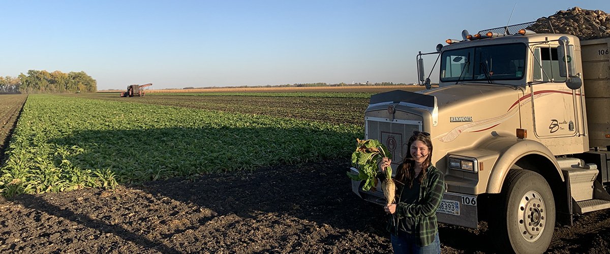 Sam Rude holding a sugar beet in front of a sugar beet field being harvested