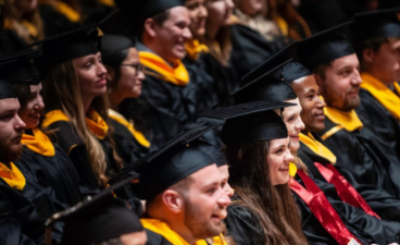 Two rows of graduate students smile and look on at a previous year's commencement ceremony.  